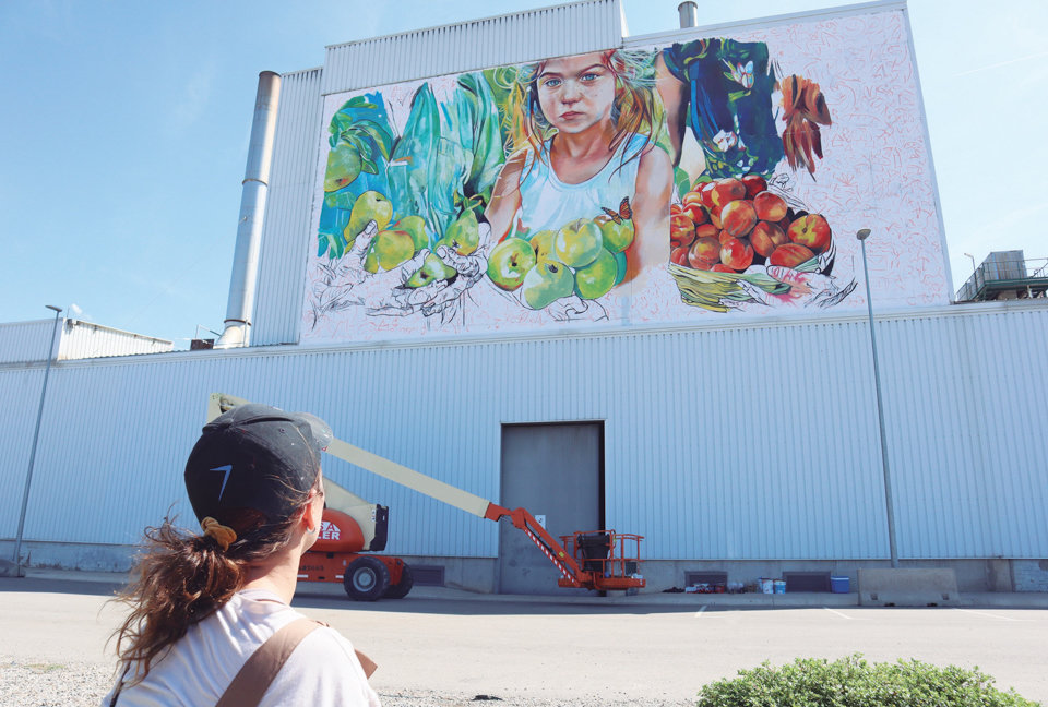 Lily Brick mira el mural que està fent a la façana d'una nau de l'empresa Nufri - Foto: Nufri