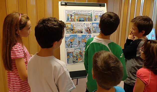 Els nens i nenes observen una tira de còmic de la publicació Cavall Fort.