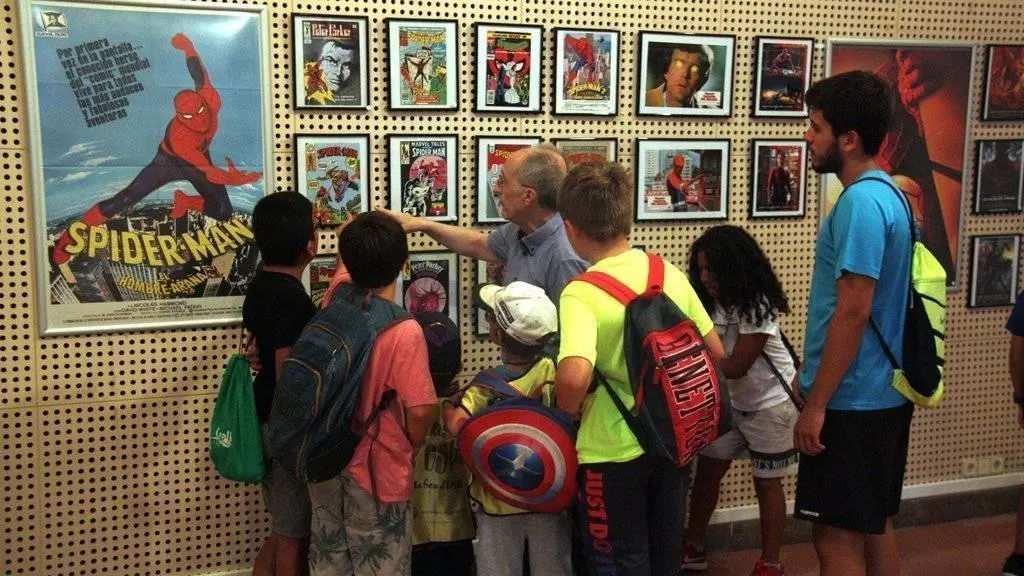 Pla americà del cinèfil i col·leccionista Josep Benavent explicant a diversos participants del casal d'estiu de la Seu d'Urgell alguns dels còmics de l'exposició 'Herois i superherois'. Imatge del 6 d'agost de 2019 (Horitzontal).