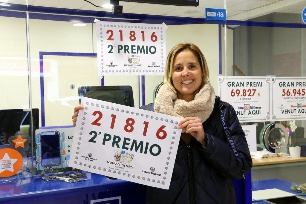 La responsable de l'administració número 14 de Pi i Margall, de Lleida, amb un cartell que indica que ha venut una sèrie del segon premi, el número 21.816. Imatge del 6 de gener del 2019. (horitzontal)