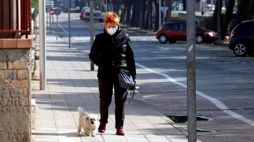 Pla mitjà on es pot veure una senyora amb màscara passejant el seu gos per l'avinguda del Canal de Mollerussa on s'hauria d'estar celebrant la Fira de Sant Josep, suspesa pel coronavirus, el 19 de març de 2020. (Horitzontal)
