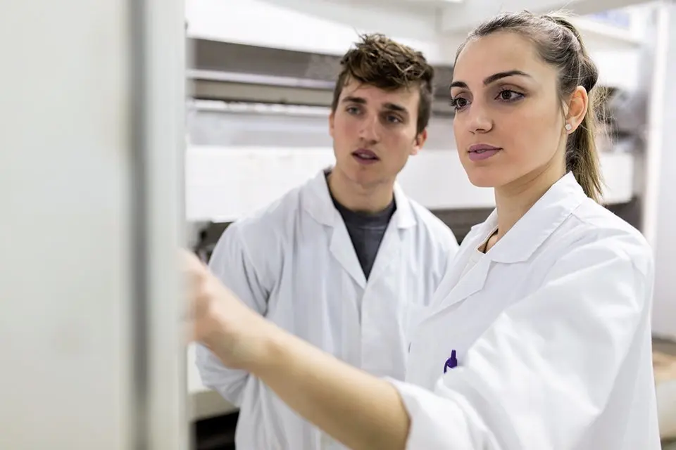 Young man touching machine in a factory and talking with her partner