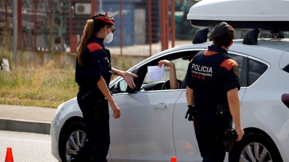 Pla mitjà on es poden veure mossos d'esquadra demanant el certificat laboral per circular al punt de control dels Alamús, el 9 de juliol de 2020. (Horitzontal)