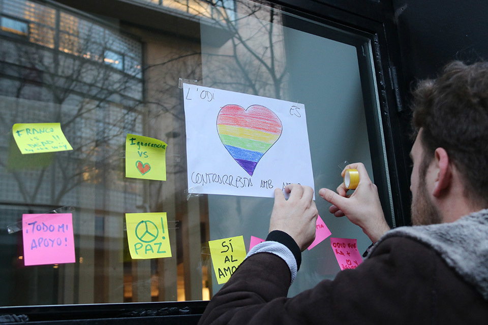 Pla mitjà d'un noi penjant un dibuix amb la bandera multicolor a l'exterior del centre LGTBI de Barcelona després que hagi rebut un atac amb amenaces de mort. Imatge del 27 de gener de 2019 (horitzontal)

Data de publicació: diumenge 27 de gener del 2019, 17:48

Autor: Gemma Sánchez