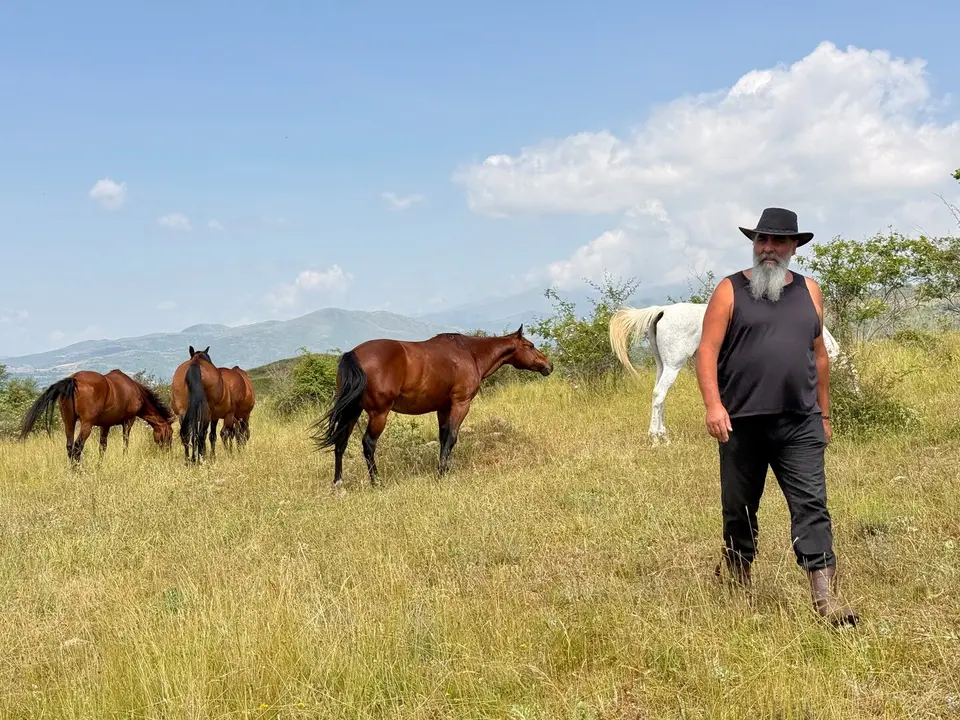 Pere Cases, el responsable de Cavalls Wakan que es dedica al retir de cavalls a Montcortès, al Pallars Sobirà, amb els cavalls al fons. Foto ACN