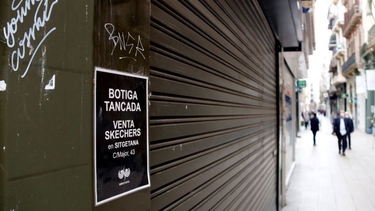 Laura Cortés El cartell d'un comerç tancat a l'Eix Comercial de Lleida en primer pla i el carrer amb gent de fons. Imatge del 20 d'octubre de 2020. (Horitzontal)