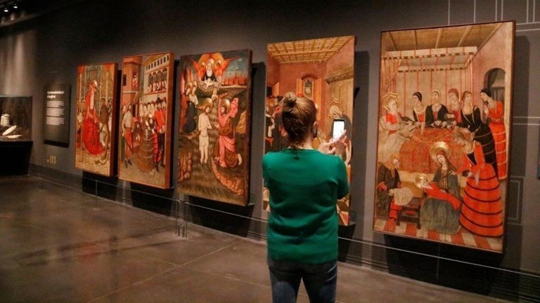 Pla obert d'una persona fotografiant cinc dels retaules que formen part de l'exposició de les sales de gòtic remodelades al Museu de Lleida. Imatge del 14 de maig de 2021. - Laura Cortés