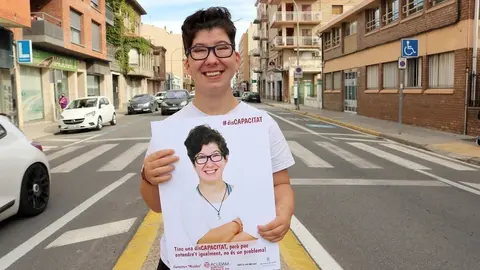 Una de les usuàries de l'ACUDAM, Desiré Palomino posant amb el seu cartell de la campanya a Mollerussa ©ACUDAM