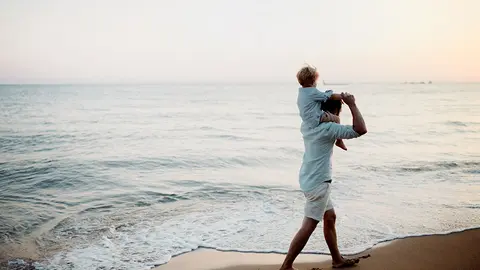 Mature father with a toddler boy walking on beach on summer holiday, having fun.