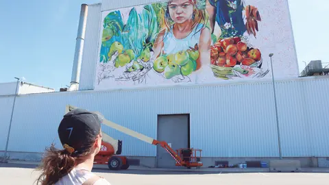 Lily Brick mira el mural que està fent a la façana d'una nau de l'empresa Nufri - Foto: Nufri