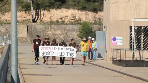 Pla general dels participants a la Marxa dels Sediments portant una pancarta que reclama una millor gestió dels sediments a les preses de l'Ebre, mentre creuen a peu la presa del pantà de Riba-roja. Imatge del 22 de juny del 2021 (horitzontal)