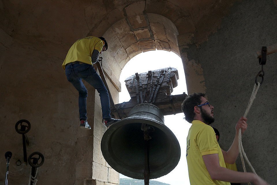 Imatge d'un jove campaner d'Os de Balaguer enfilat a una gran campana de l'església