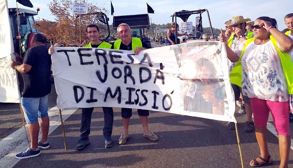 Un grup de manifestants afectats pels focs del juny mostrant una pancarta que demana la dimissió de la consellera Teresa Jordà