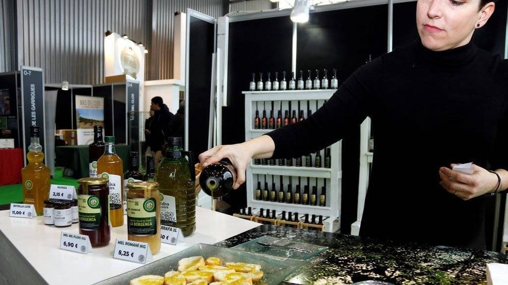 Pla mitjà on es pot veure una expositora de la 56a Fira de l'Oli Verge Extra de les Borges Blanques posant oli a unes llesques de pa, el 18 de gener de 2019. (Horitzontal)