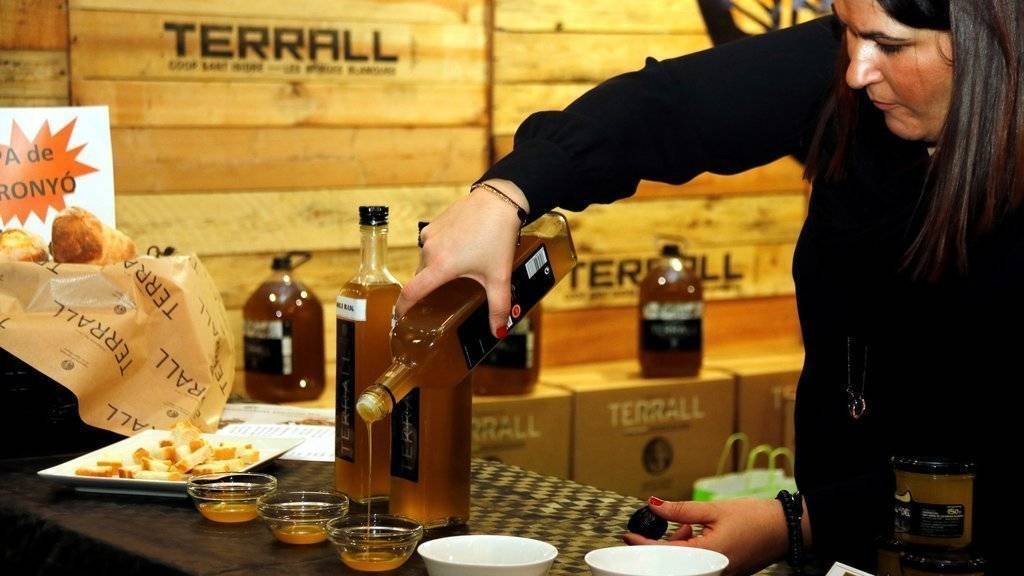 Pla mitjà on es pot veure una expositora de la 56a Fira de l'Oli Verge Extra de les Borges Blanques servint oli d'una ampolla en un recipient, el 18 de gener de 2019. (Horitzontal)