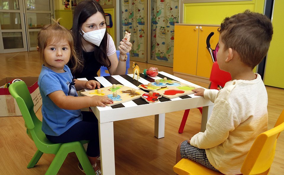 Pla mitjà on es pot veure una professora i dos infants a l'Escola Bressol de Golmés el dia de la reobertura després del tancament per la covid-19, el 8 de juny de 2020. (Horitzontal)