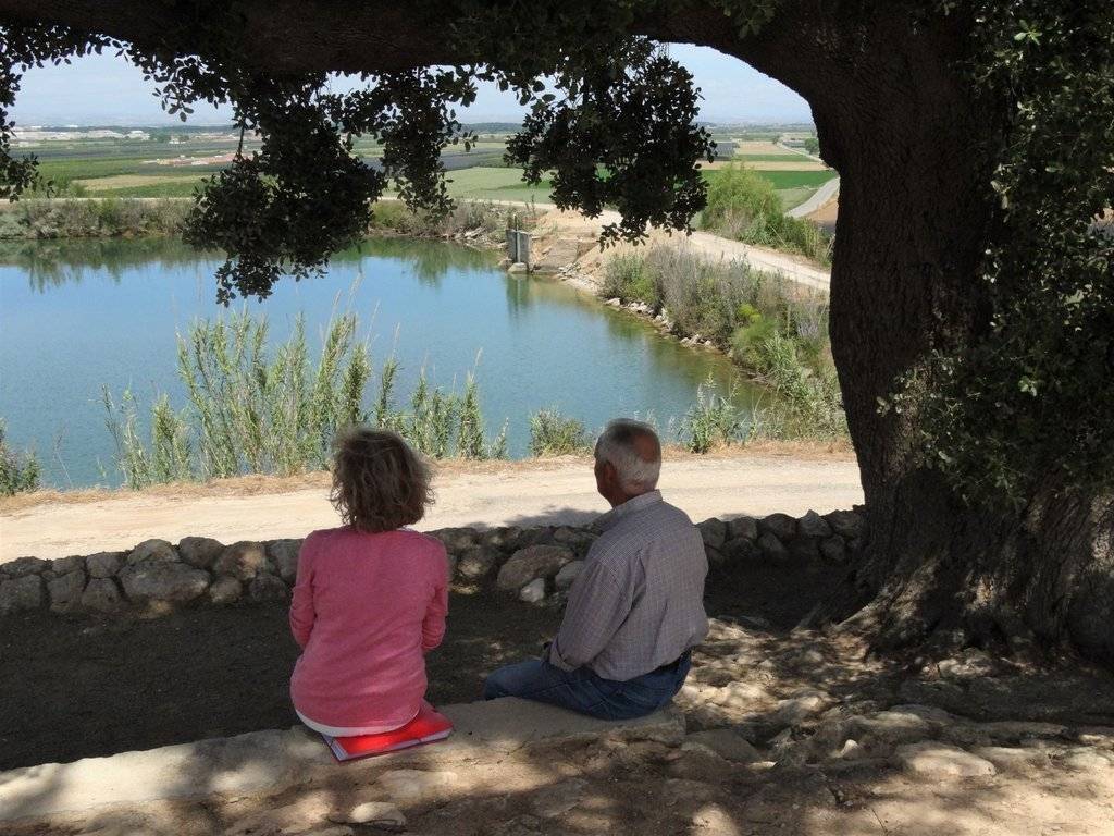 Dolors Sans i Xavier Soberà asseguts en un banc de pedra sota l'alzina, el juny de 2021 - Foto de Marina Pallàs Barta